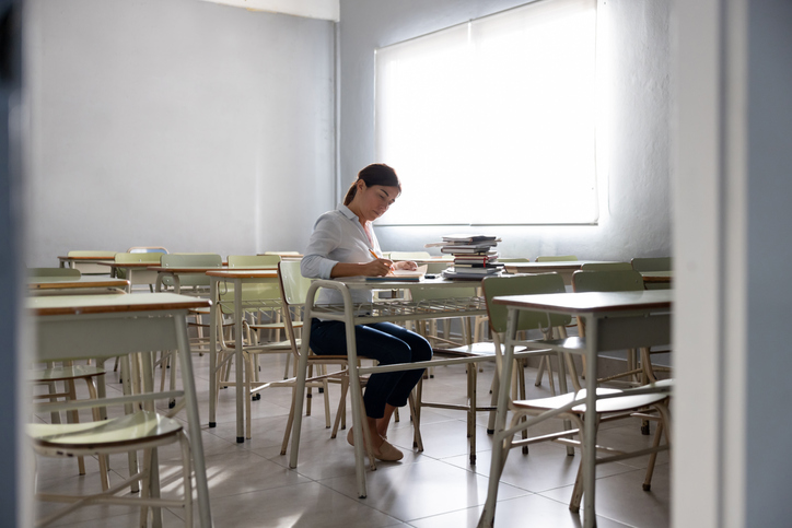 Teacher burnout as a teacher corrects papers in an empty classroom
